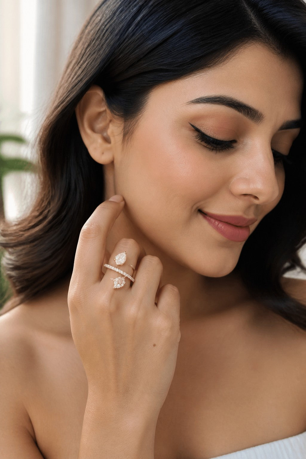A close-up lifestyle shot of a woman wearing a delicate gold ring with a clear marquise-cut gemstone on her finger, with her hand gently touching her face.