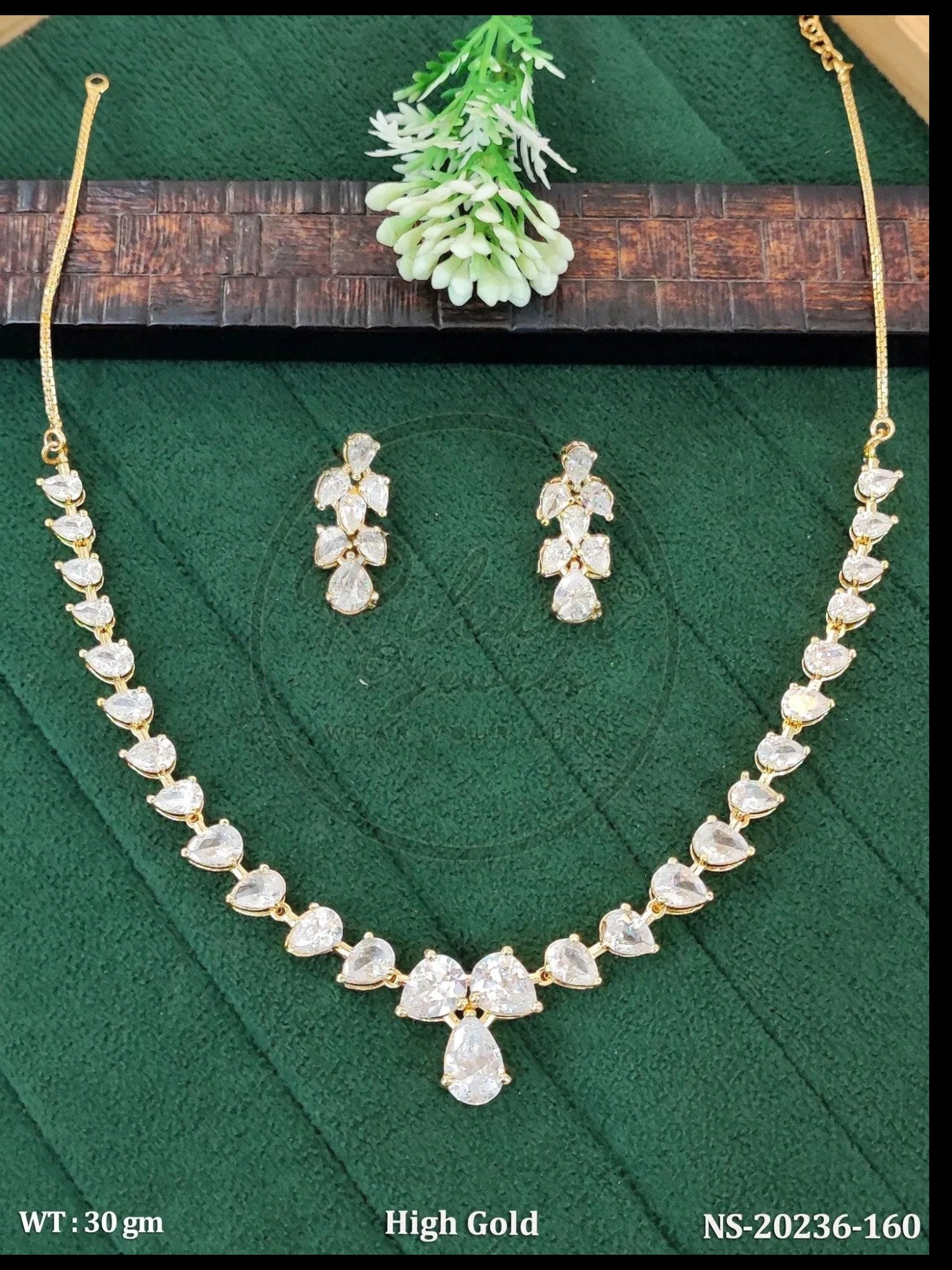 Rihum Jewels gold-plated necklace and earring set with pear-cut white cubic zirconia stones on a green background.