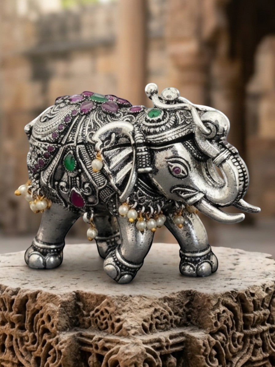 Rihum Jewels handcrafted oxidized silver elephant figurine with ruby, emerald, and pearl accents on a stone pedestal.