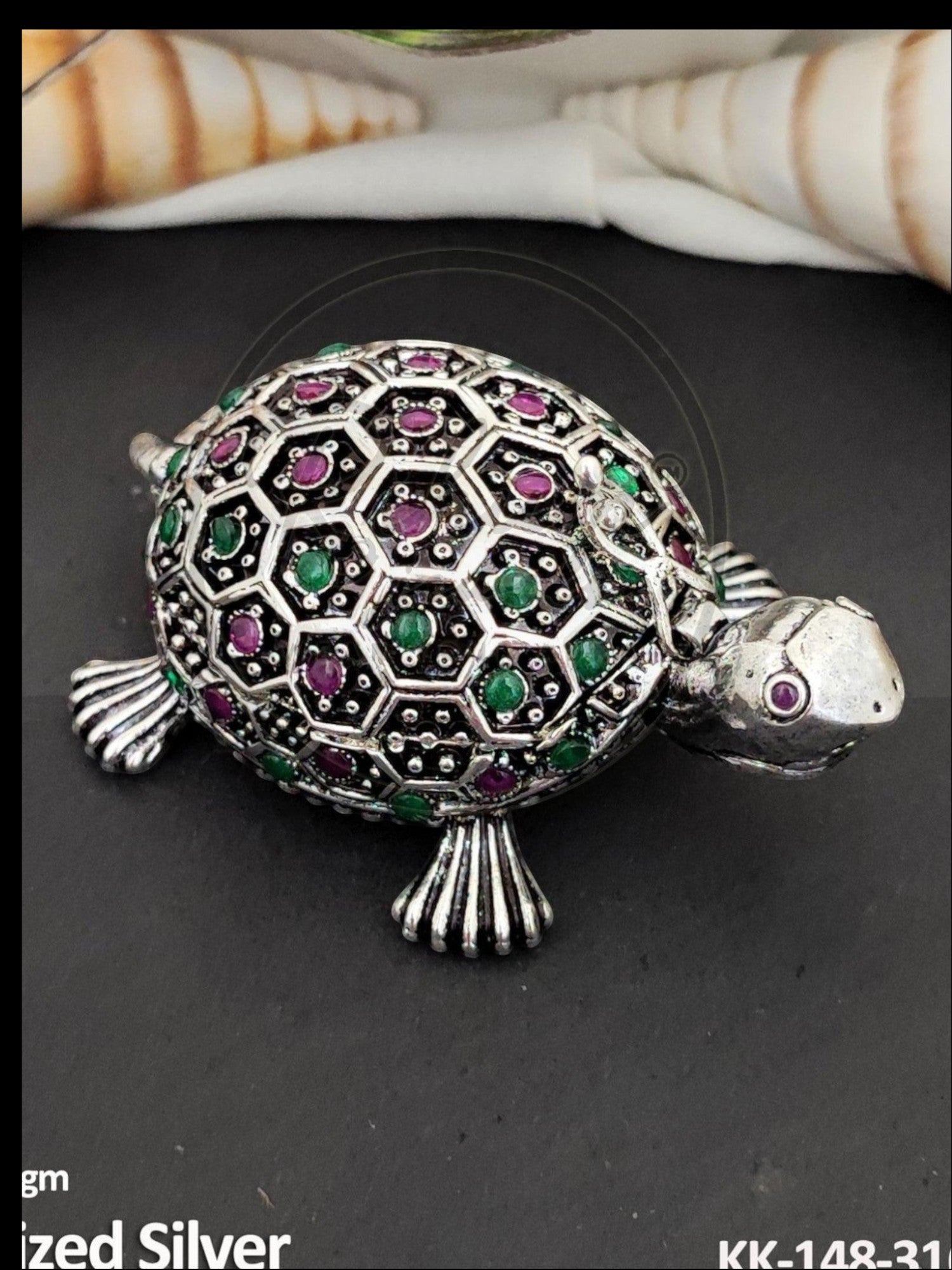 Rihum Jewels handcrafted oxidized silver tortoise sindoor box with ruby and emerald stone accents on a black surface.